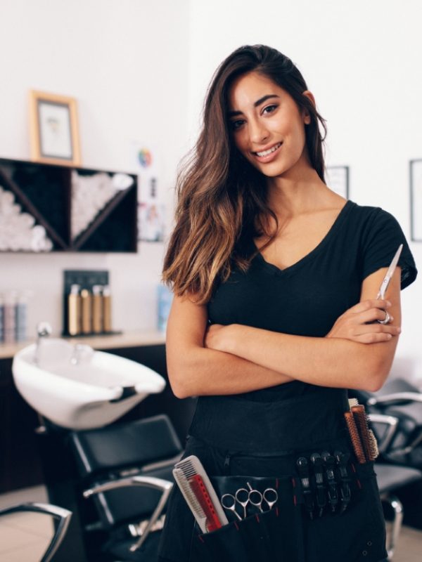 Female hairdresser in salon holding scissors in hand. Smiling young hairdresser standing in salon.