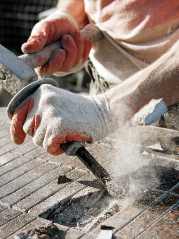 Stone carver in gloves working with a hammer and chisel on a marble slab. heavy handwork. production of monuments from marble. working with natural stone