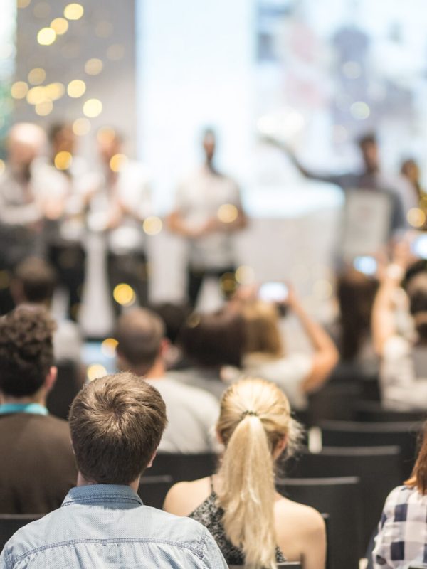 Young business team receiving award prize at best business project competition event. Business and entrepreneurship award ceremony theme. Focus on unrecognizable people in audience.