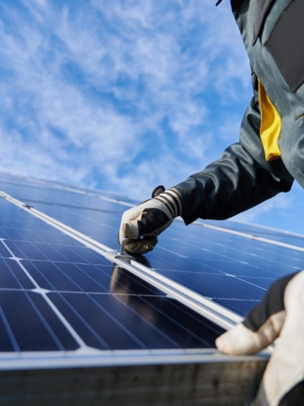 Close up of man technician in work gloves installing stand-alone photovoltaic solar panel system under beautiful blue sky with clouds. Concept of alternative energy and power sustainable resources.