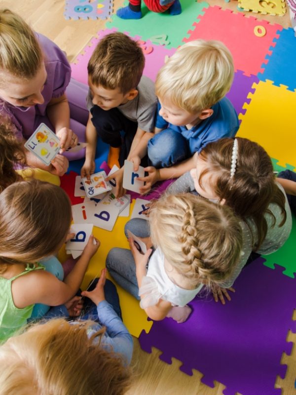 Group of kindergarten kids sitting closely on a floor together with teacher, providing group work. Children learning to cooperate while solving tasks.
